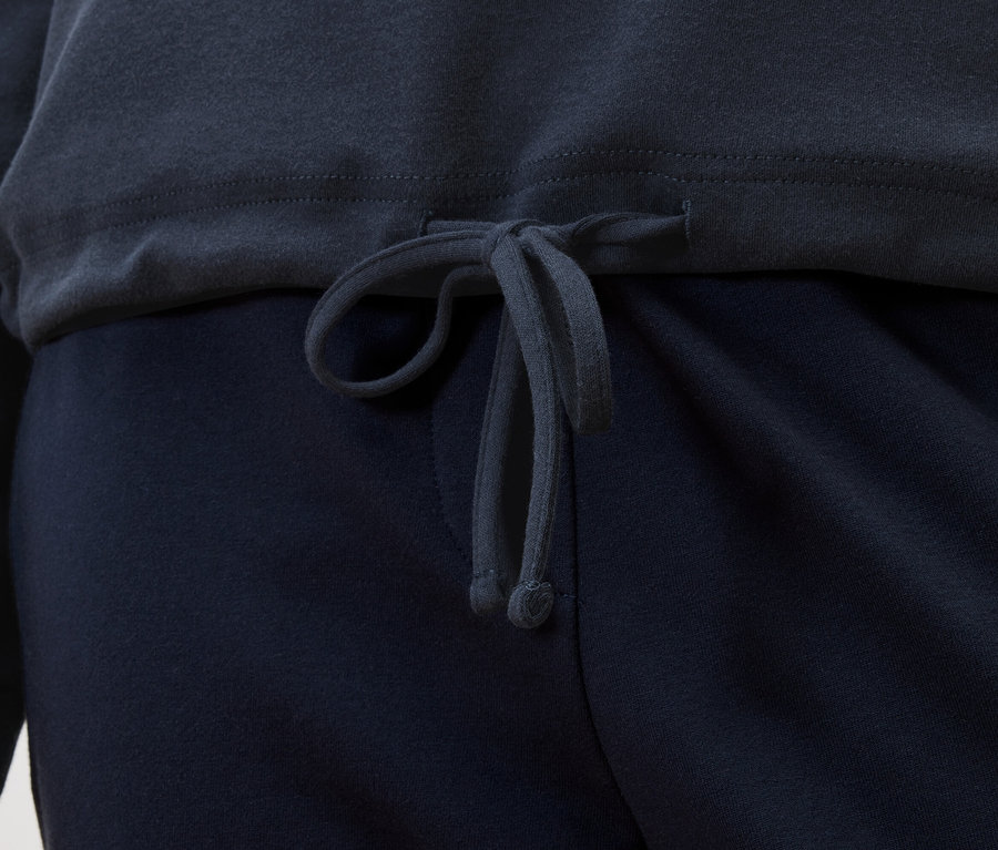 Detailansicht eines dunkelblauen Oberteils mit Kordelzug über einer dunkelblauen Hose.