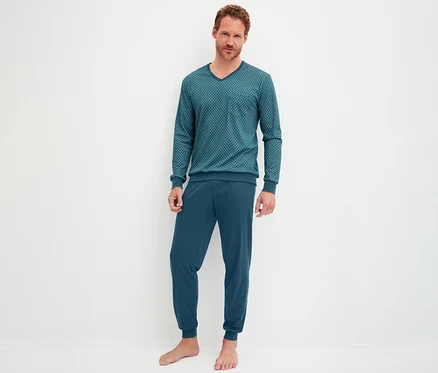Mann steht barfuß und trägt ein CALIDA Streamline Pyjama-Set mit Bündchen. Das Set besteht aus einem petrolfarbenen V-Ausschnitt-Oberteil mit geometrischem Muster und einer passenden Hose mit Bündchen.