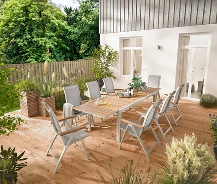 Ein ausziehbarer Gartentisch aus Aluminium »Liska« mit ca. 200–300 cm Länge steht auf einer Holzterrasse, umgeben von sechs Hochlehnern »Liska« mit verstellbarer Rückenlehne. Zwei Pflanzsäulen »Tinus« und fünf LED-Gartenfackeln sind ebenfalls sichtbar.