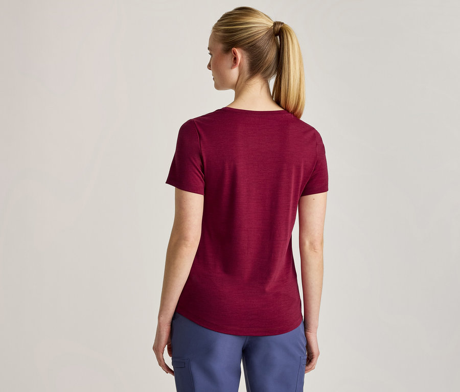 Eine Frau von hinten, die ein weinrotes Kurzarm-T-Shirt und eine blaue Hose trägt. Ihr blondes Haar ist zu einem Pferdeschwanz gebunden.