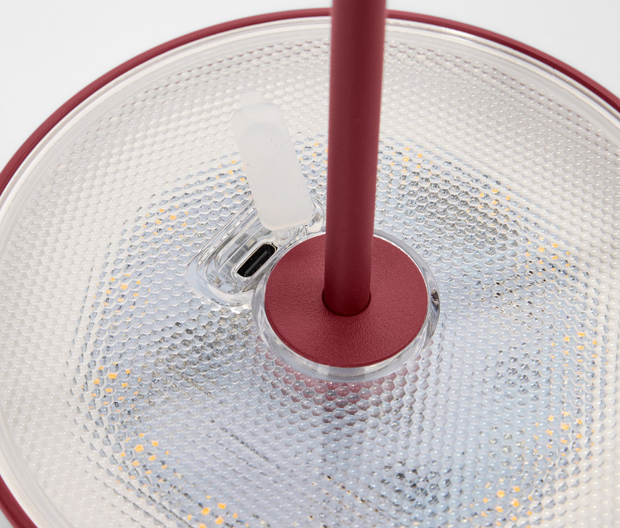 Detailansicht einer Lampe mit rotem Rand und Ständer, die auf einer strukturierten Oberfläche steht.