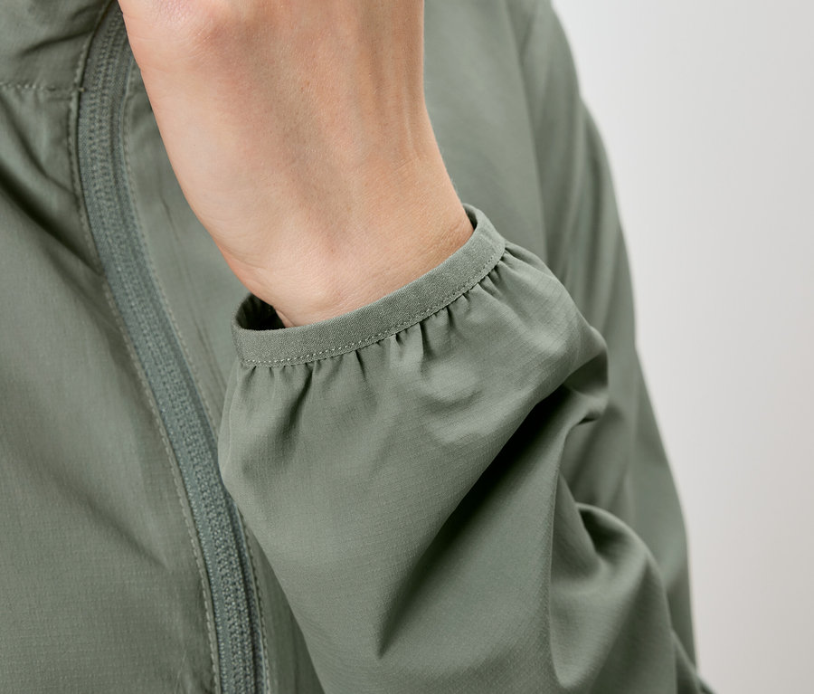 Nahaufnahme einer Person, die eine olivgrüne Jacke trägt, wobei die Hand in der Tasche steckt und der Ärmel gerafft ist.