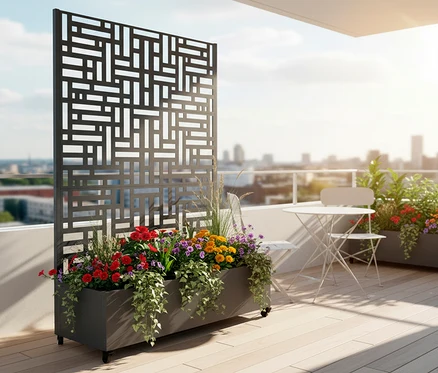 Aufnahme eines grauen Pflanzgefäßes mit bunten Blumen und einem Metallgitter auf einem Balkon mit Tisch und Stühlen.