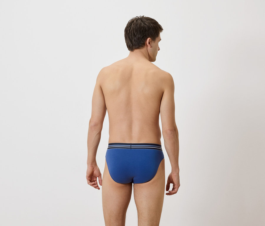 Rückansicht eines Mannes mit blauen Slips mit einem blau-weiß gestreiften Bund vor einem schlichten Hintergrund.