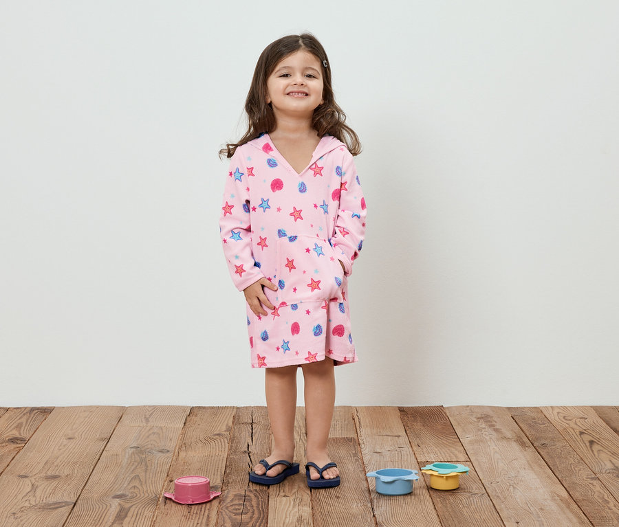 Mädchen mit braunen Haaren trägt einen rosafarbenen Bademantel mit Sternen und Muscheln.