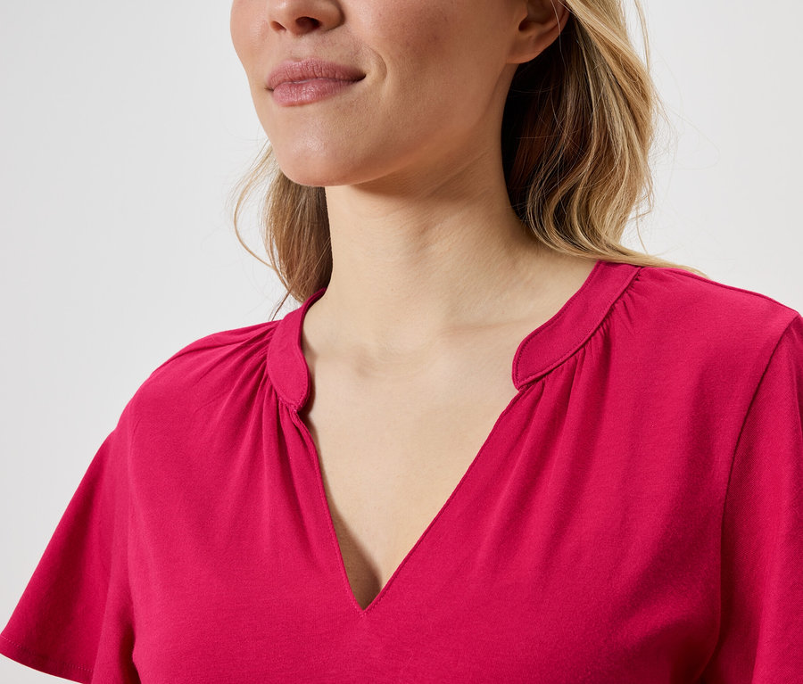 Nahaufnahme einer Frau mit blonden Haaren, die ein pinkes Oberteil mit V-Ausschnitt trägt.