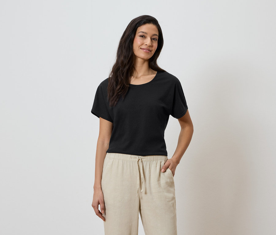 Frau mit schwarzem T-Shirt und beiger Hose mit der Hand in der Hosentasche.
