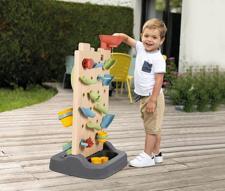 Junge gießt Wasser in die Smoby Life Activity Wall. Das Wasser läuft durch die verschiedenen Elemente.