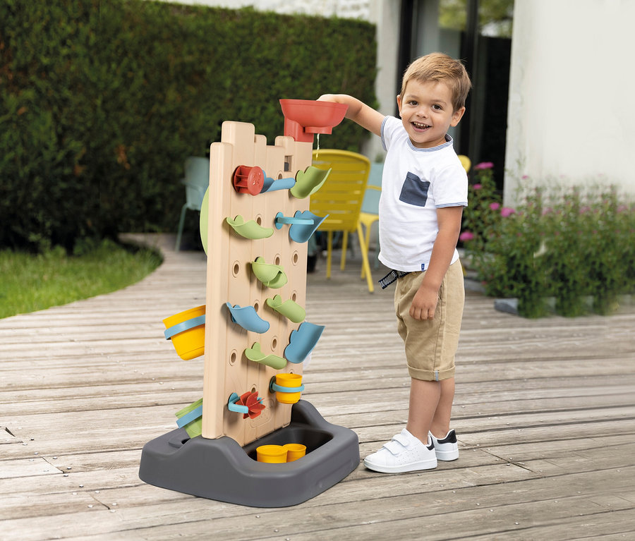 Junge gießt Wasser in die Smoby Life Activity Wall. Das Wasser läuft durch die verschiedenen Elemente.