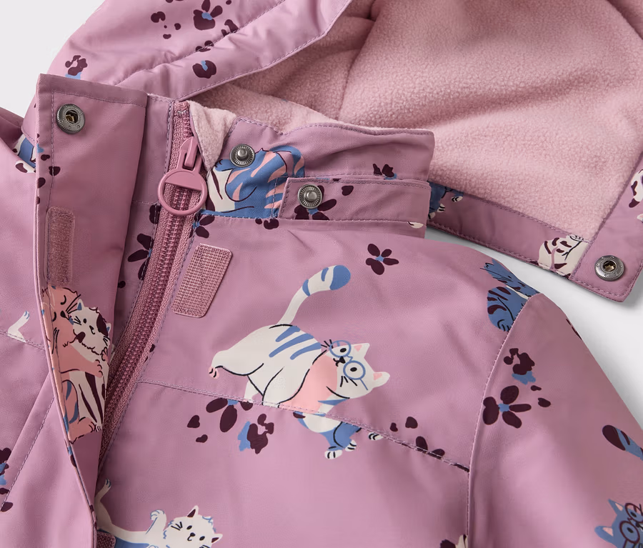 Nahaufnahme einer lila Jacke mit Katzen- und Blumenmuster, Reißverschluss und Kapuze mit rosa Fleecefutter.