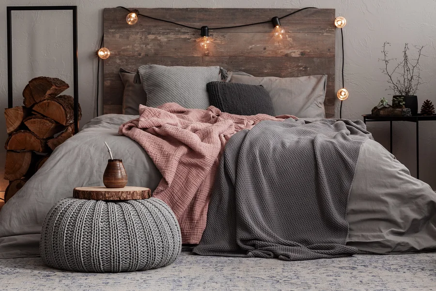 Ein Schlafzimmer mit einem Bett mit grauer Bettwäsche, einer rosa Decke und einer grauen Strickdecke. Auf dem Boden liegt ein gemusterter Teppich.