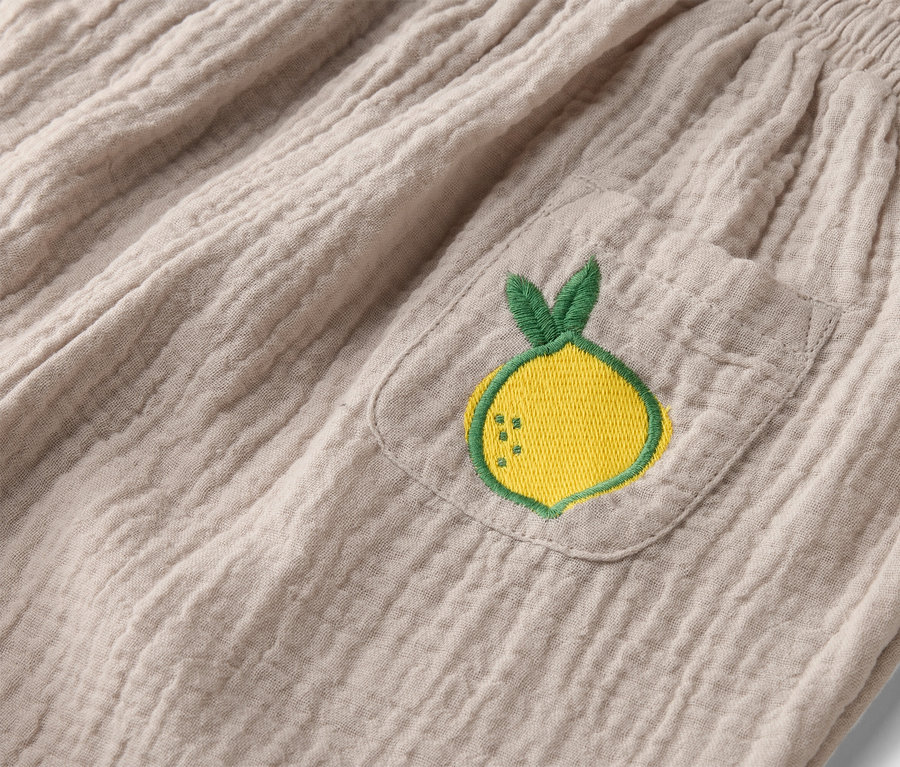 Nahaufnahme von beigen Stoffhosen mit elastischem Bund und aufgesetzter Tasche mit gelber Zitronenstickerei.