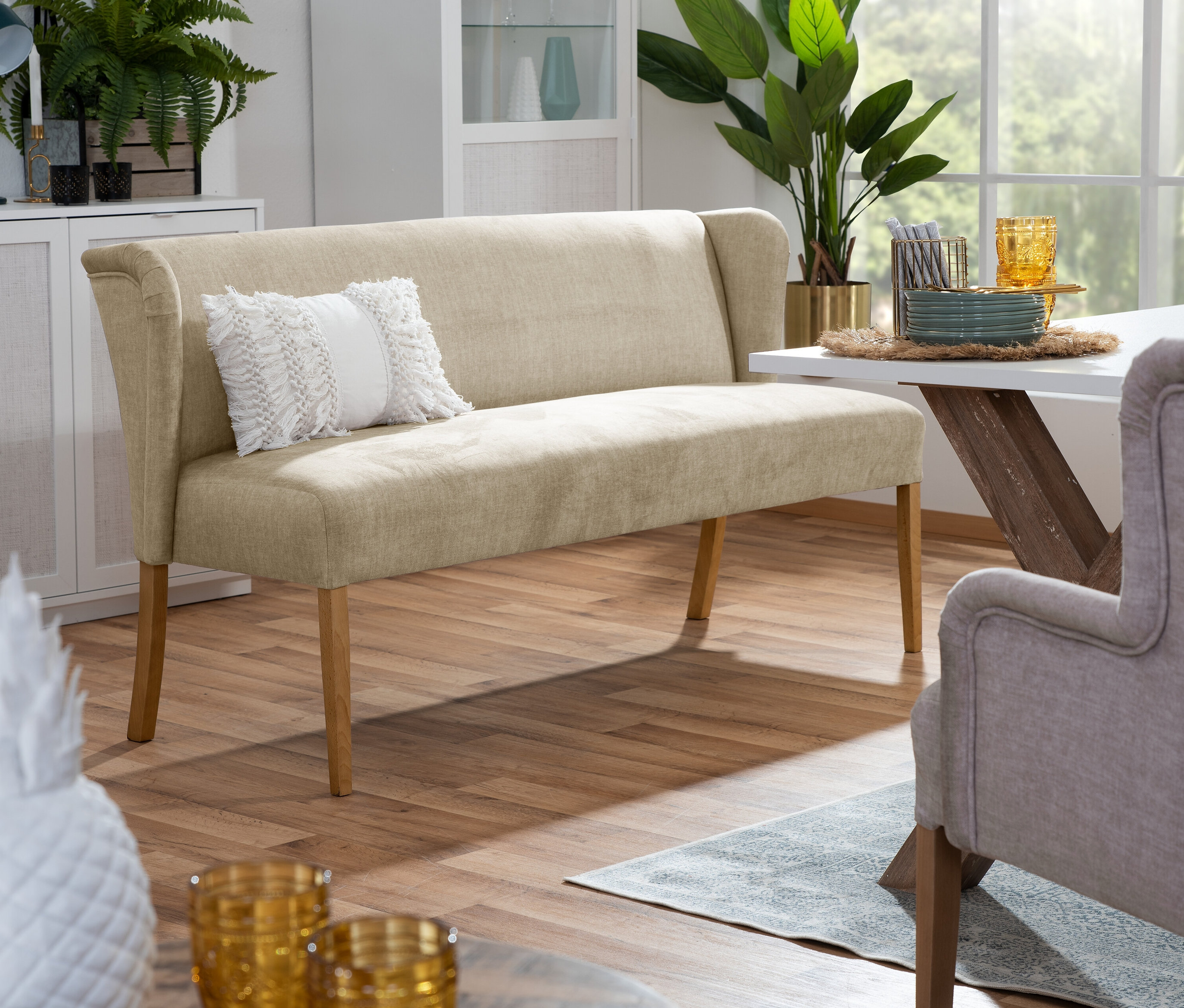 Beige Polsterbank »Hendrick« mit Kissen steht neben einem Esstisch in einem Wohnzimmer.