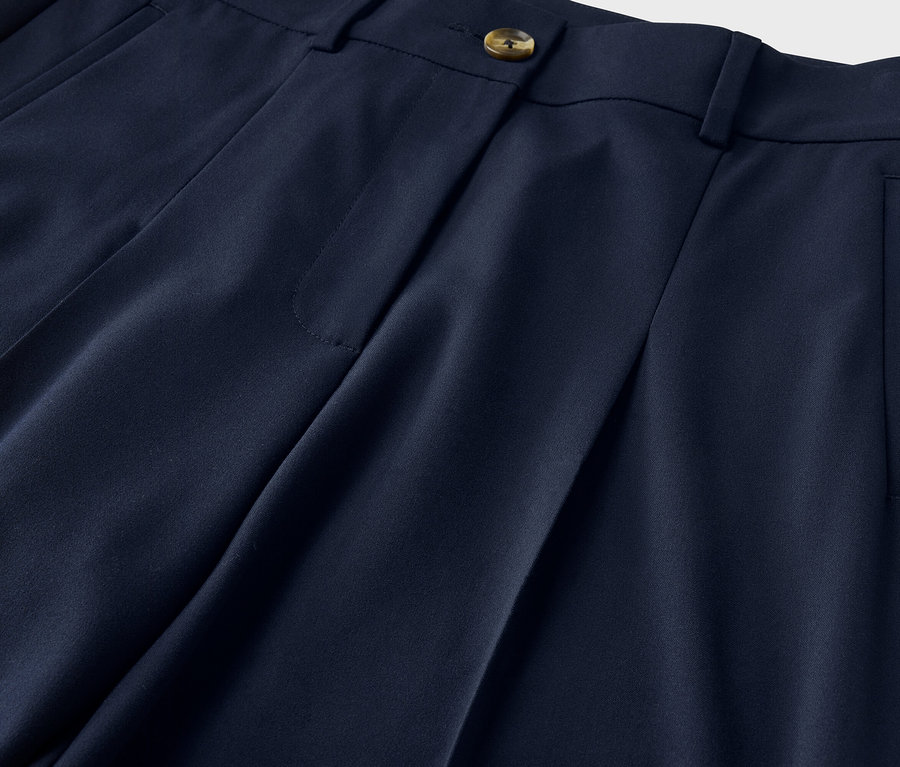 Nahaufnahme einer marineblauen Hose mit Bundfalten, Knopf und Tascheneingriff.