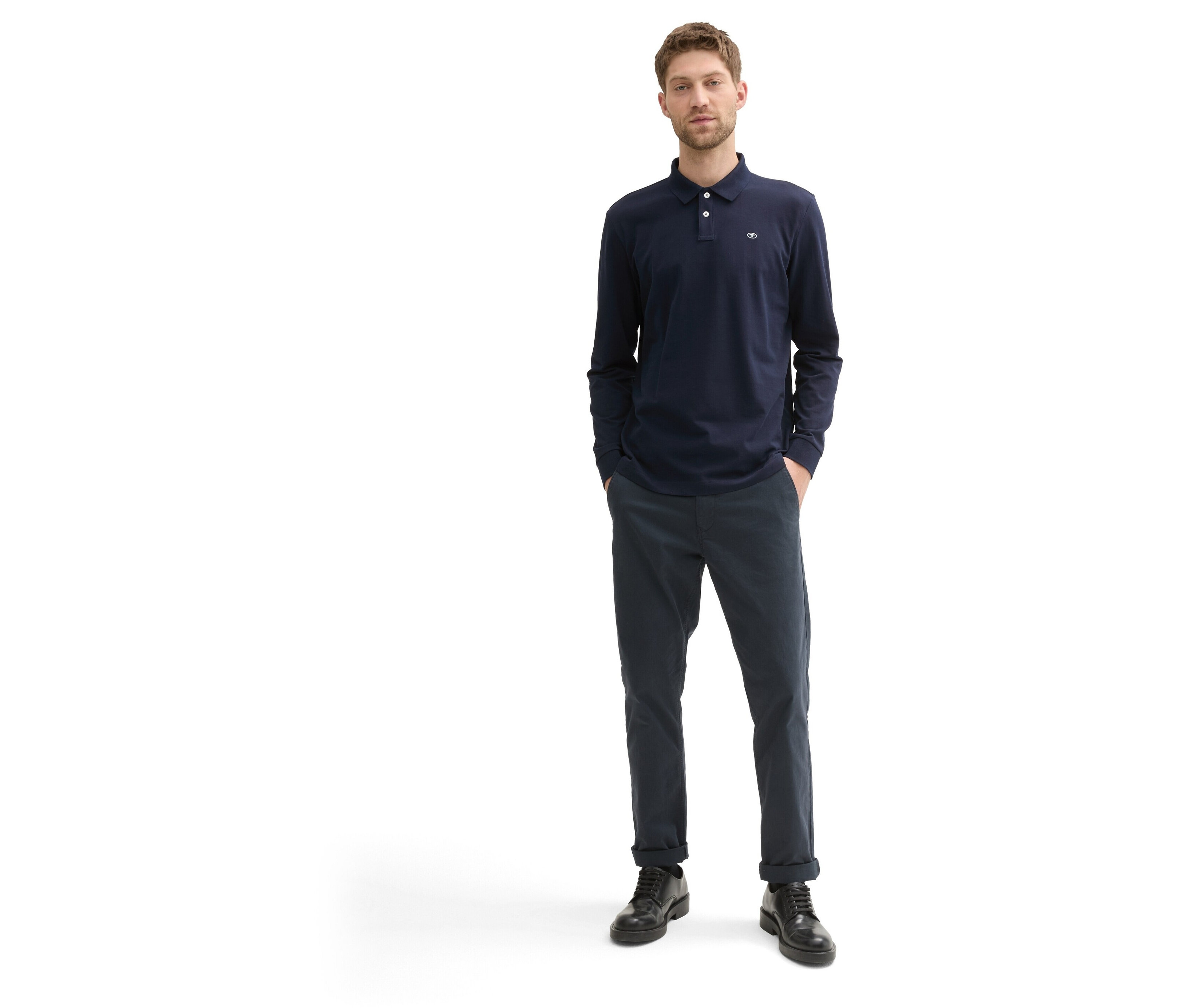 Mann steht und trägt ein dunkelblaues Langarm-Poloshirt, eine dunkelblaue Hose und schwarze Schuhe.