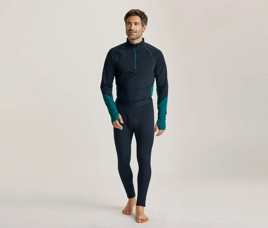 Barfüßiger Mann in dunkelblauem Langarmshirt mit türkisen Akzenten und passenden Leggings, der nach links blickt.