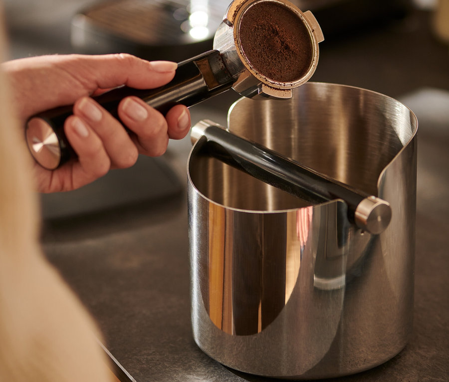 Hand hält Kaffeeträger über glänzender Knock Box.