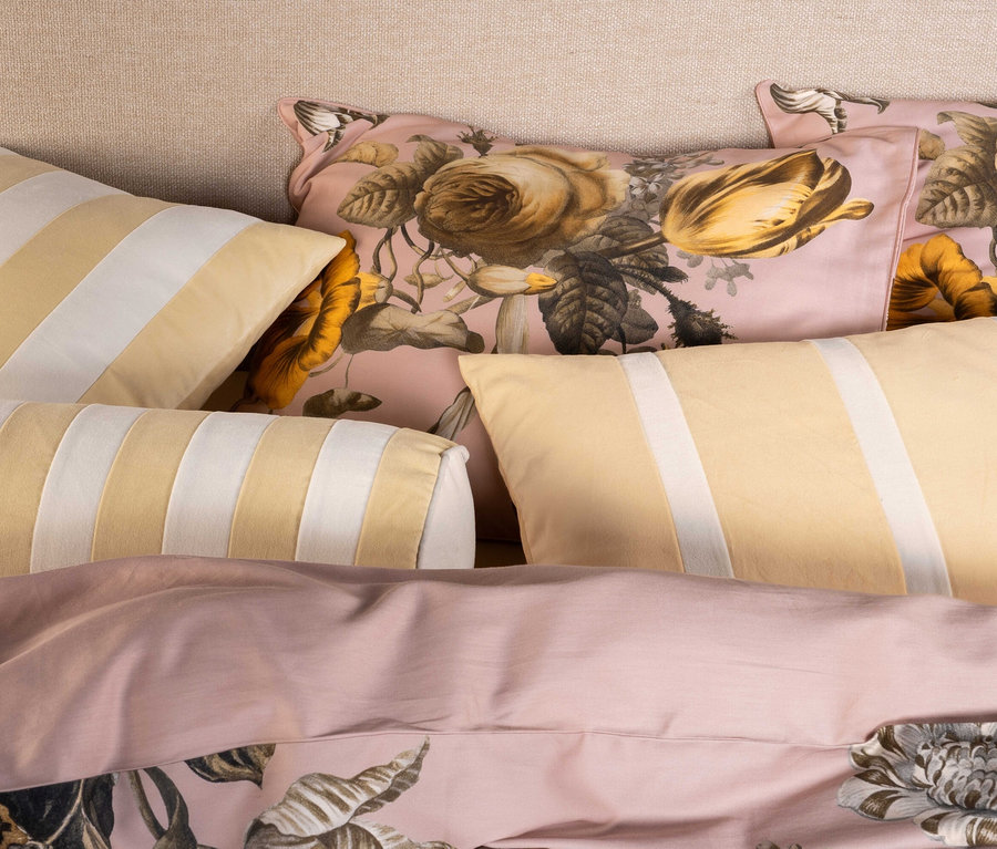 Nahaufnahme von Kissen und Bettwäsche. Die Kissen haben gelbe und weiße Streifen oder ein florales Muster auf rosa Hintergrund. Die Bettwäsche ist rosa mit einem floralen Muster.