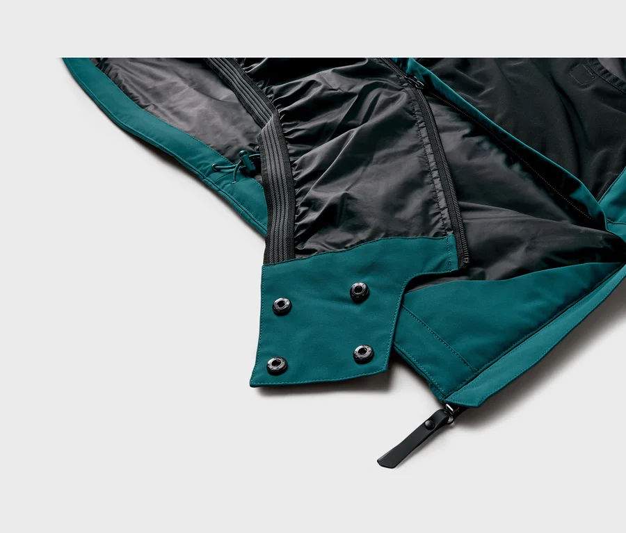 Nahaufnahme der Innenseite einer tealfarbenen und schwarzen Jacke mit Reißverschluss, vier Druckknöpfen und Kordelzug.