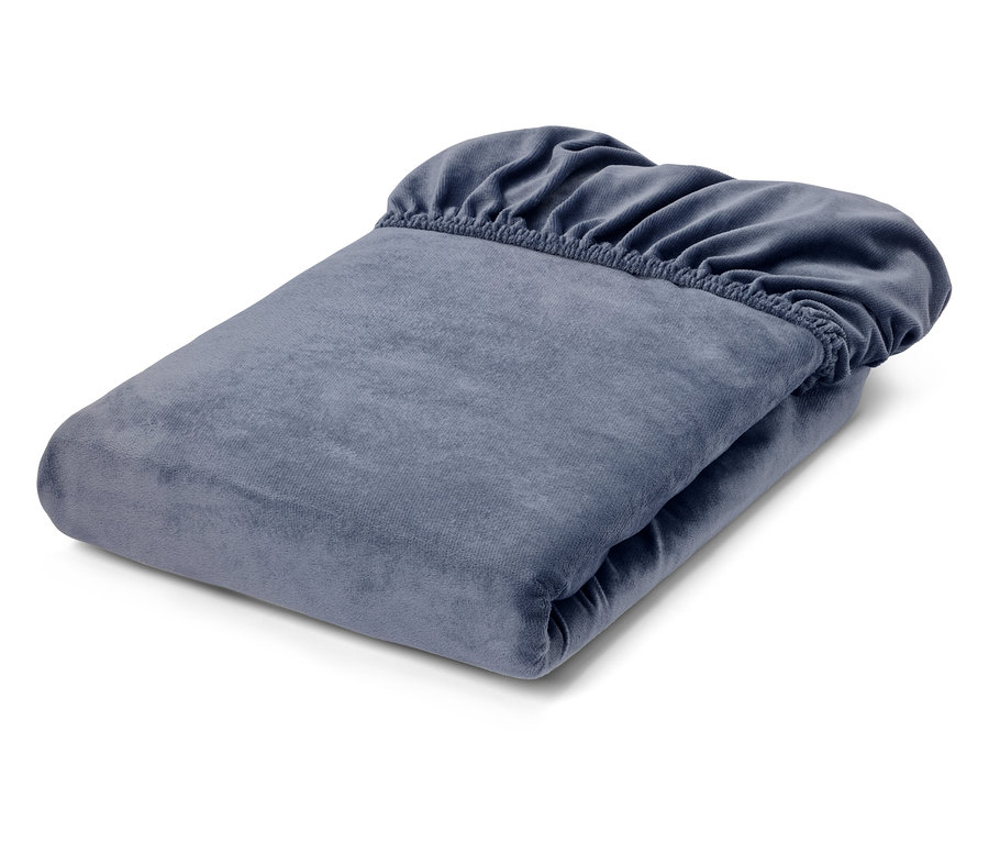 Ein sauber gefaltetes, blau-graues Spannbettlaken aus weichem Veloursstoff, dessen Gummizug am oberen Rand sichtbar ist.