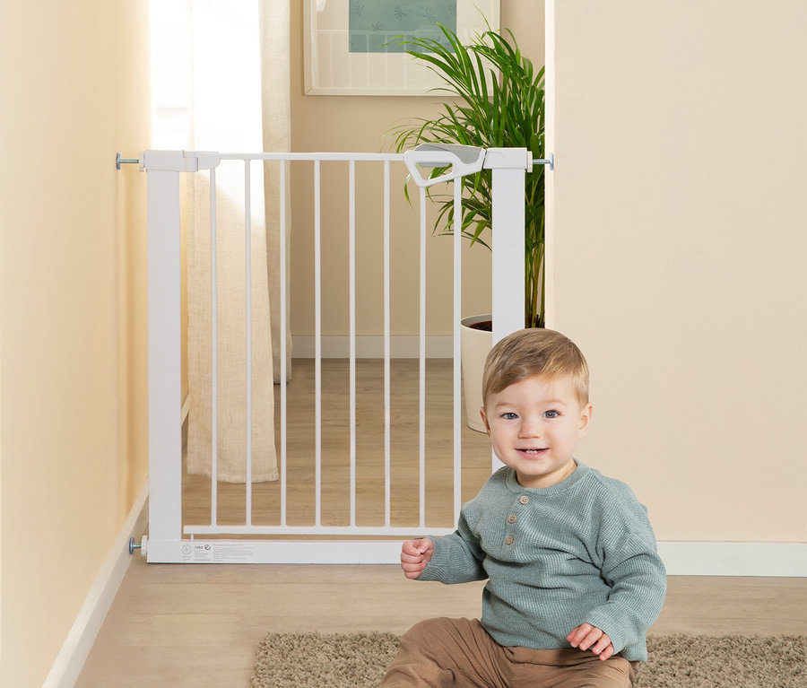 Ein lächelndes Baby sitzt auf einem Teppich vor einem weißen roba easySafe+ Tür-und-Treppen-Schutzgitter, das in einem Türrahmen installiert ist.