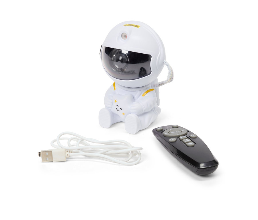 Ein weißer Nachthimmelprojektor in Form eines Astronauten sitzt neben einer schwarzen Fernbedienung und einem weißen USB-Kabel.