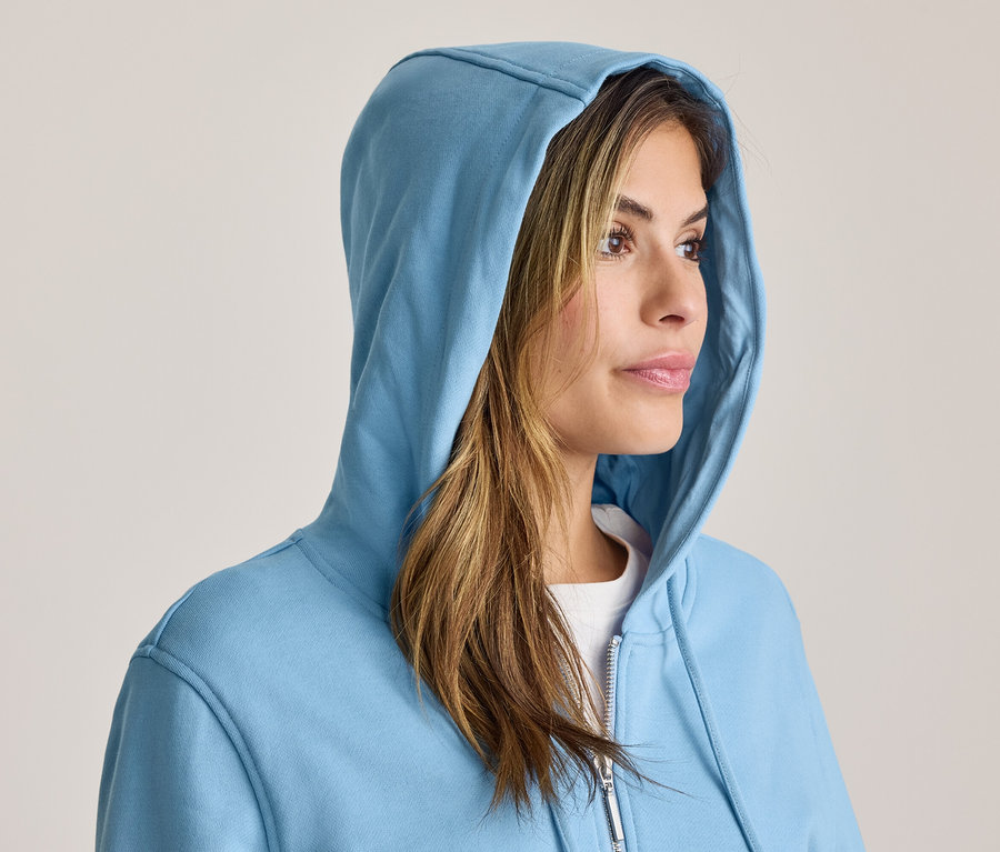 Frau in einem blauen Kapuzenpullover, die nach rechts blickt, ihr braunes Haar ist sichtbar.
