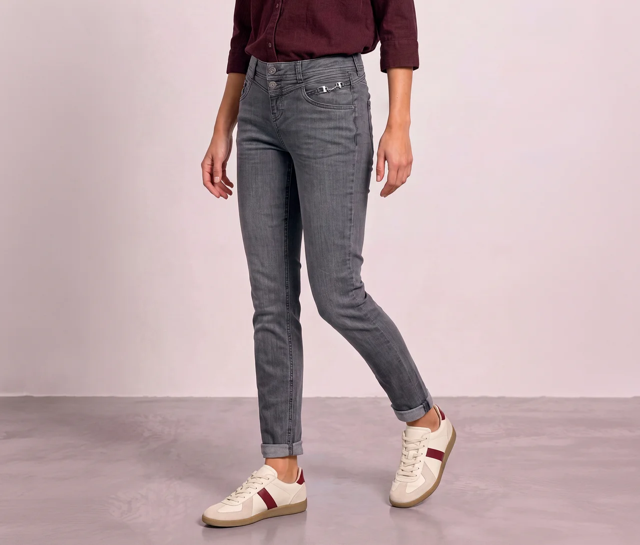 Eine Person trägt graue Street One Jeans, die an den Knöcheln umgeschlagen sind, dazu ein weinrotes Hemd und weiße Sneaker mit roten Streifen.