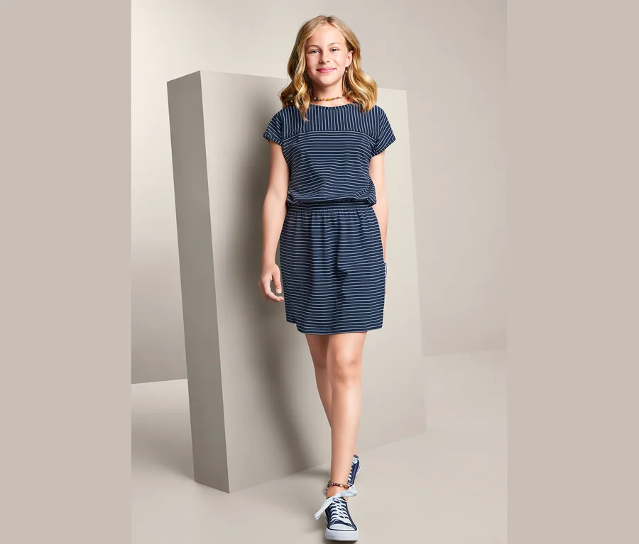 Mädchen posiert stehend in einem gestreiften Jerseykleid.