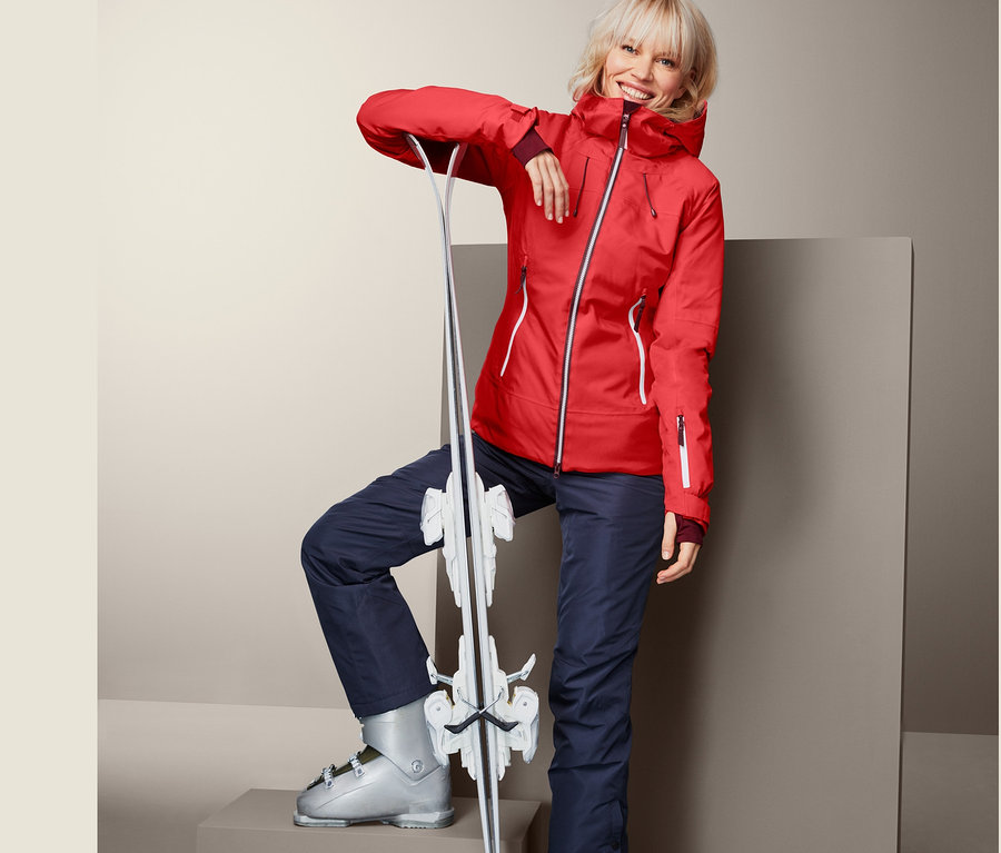 Frau in roter Skijacke, die sich an Ski anlehnt.
