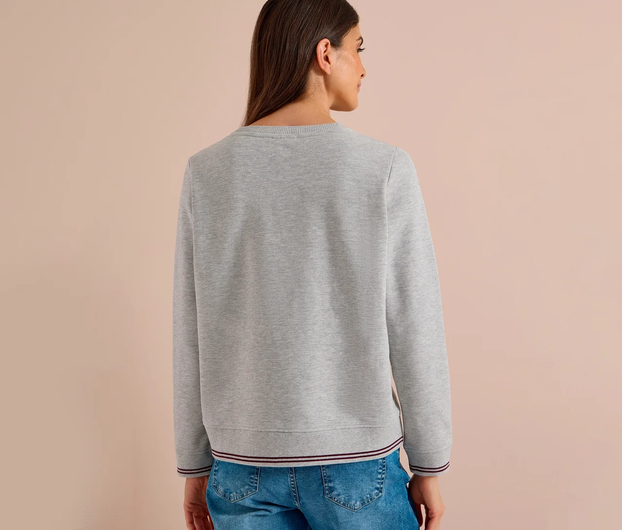 Frau von hinten in einem grauen CECIL Sweatshirt mit gestreiftem Rippbündchen und Ärmelbündchen, kombiniert mit blauen Jeans.