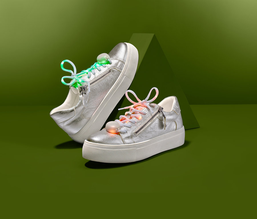 Zwei silberne Turnschuhe mit LED-Leucht-Schnürsenkeln auf grünem Hintergrund.