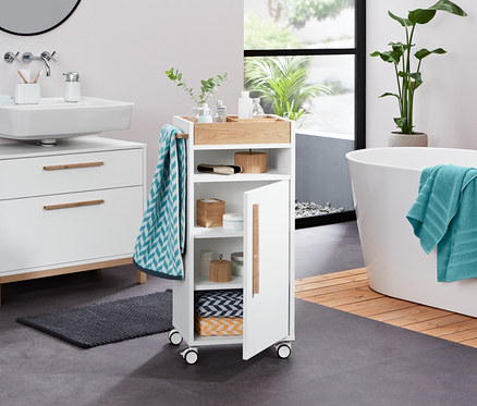 Im Badezimmer stehen ein weißer Waschbeckenunterschrank »Eklund« mit zwei Schubladen, ein Utensilo, ein Seifenspender, ein Frottier-Badetuch, 2 Jacquard-Handtücher, 2 Frottier-Handtücher (anthrazit), 2 Dosen aus Bambus, 2 LED-Dekosteine und ein Bad-Beistellwagen »Eklund«.