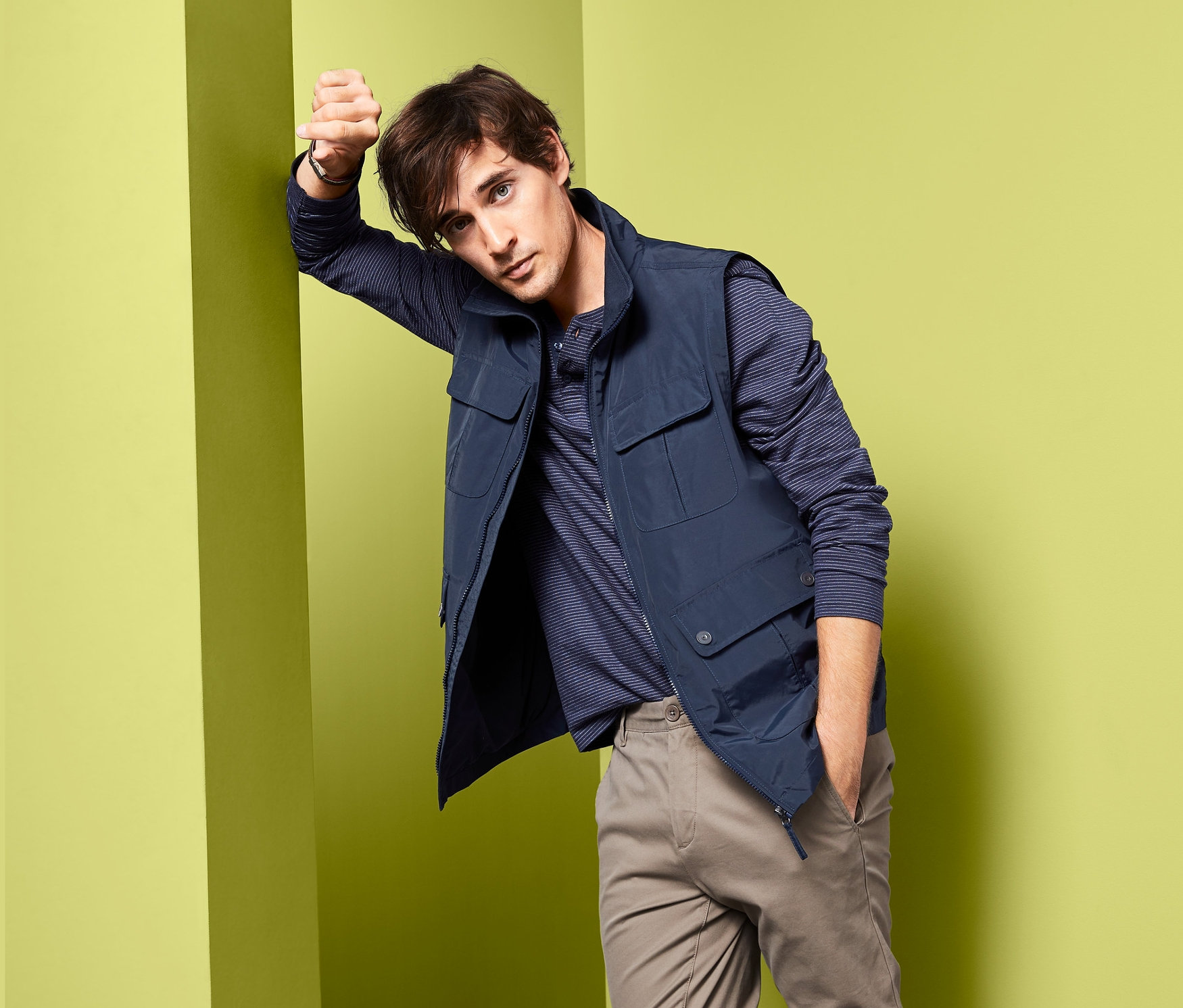 Mann lehnt an Wand und trägt Weste.