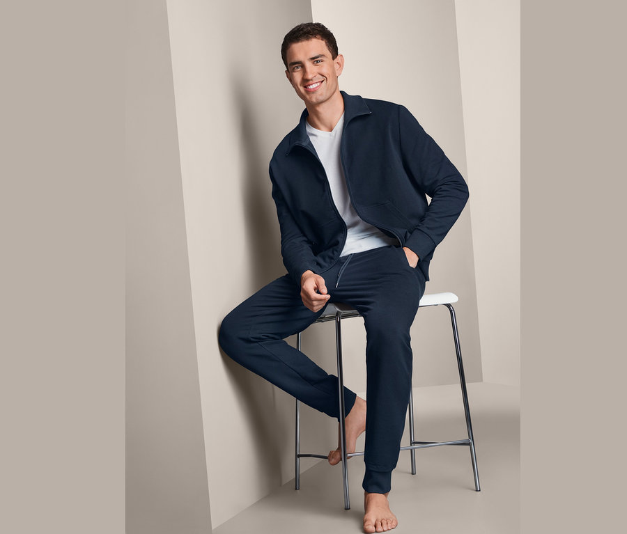 Mann sitzt auf einem Hocker und trägt einen marineblauen Homewear-Anzug.