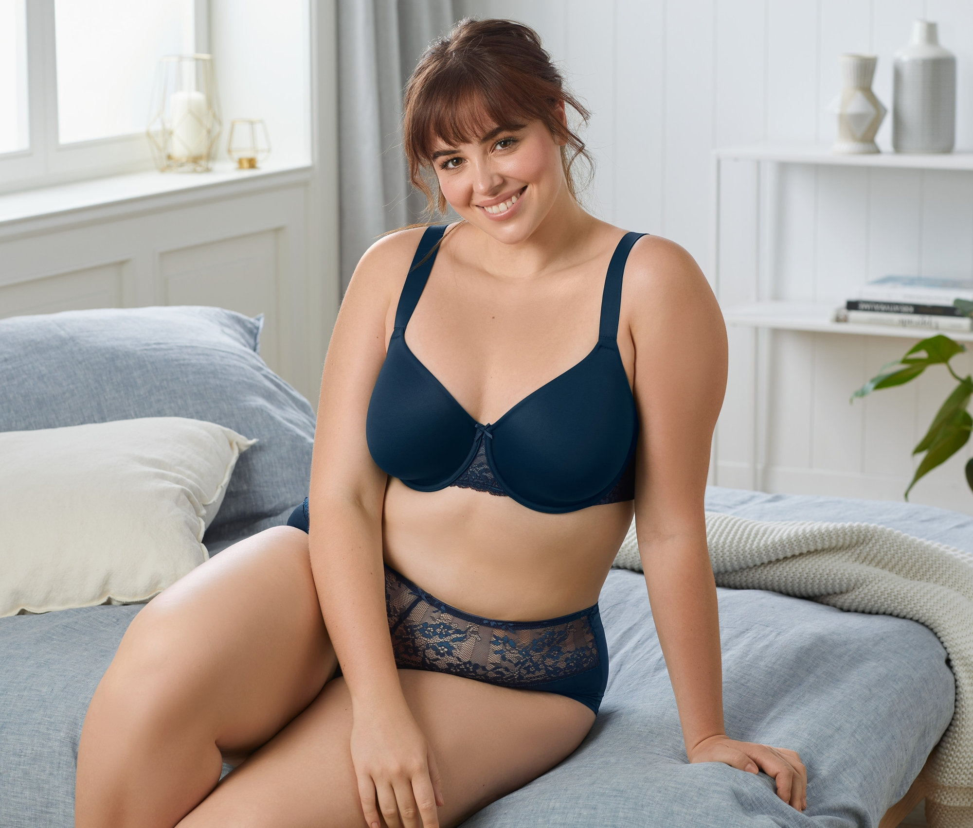 Frau sitzt auf einem Bett und trägt einen dunkelblauen Bügel-BH.