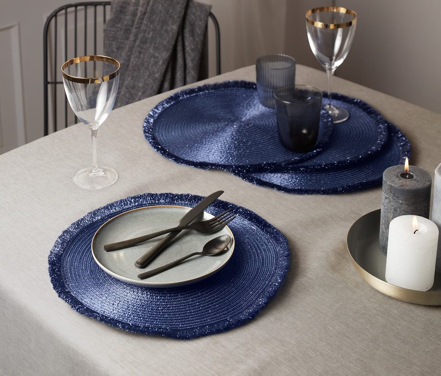 Gedeckter Tisch mit 4 blau-lila Platzsets, Teller und Besteck.