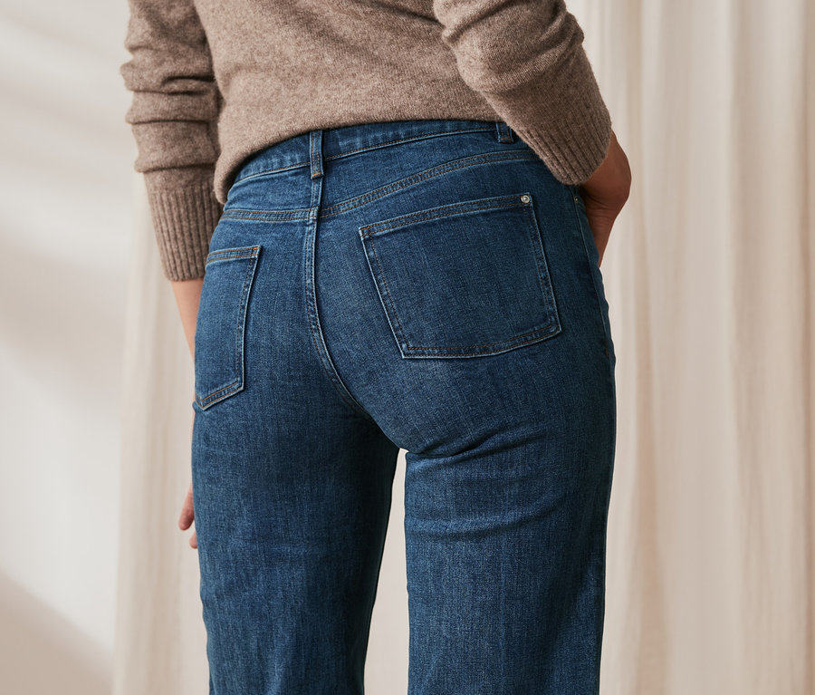 Rückansicht einer Frau mit braunem Pullover und Jeans in verkürzter Länge.