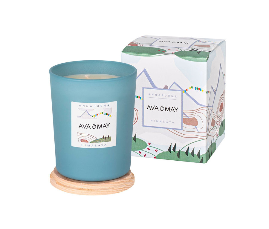 Eine blaue Duftkerze »Himalaya« von Ava & May steht auf einem Holzuntersetzer neben der Verpackung.