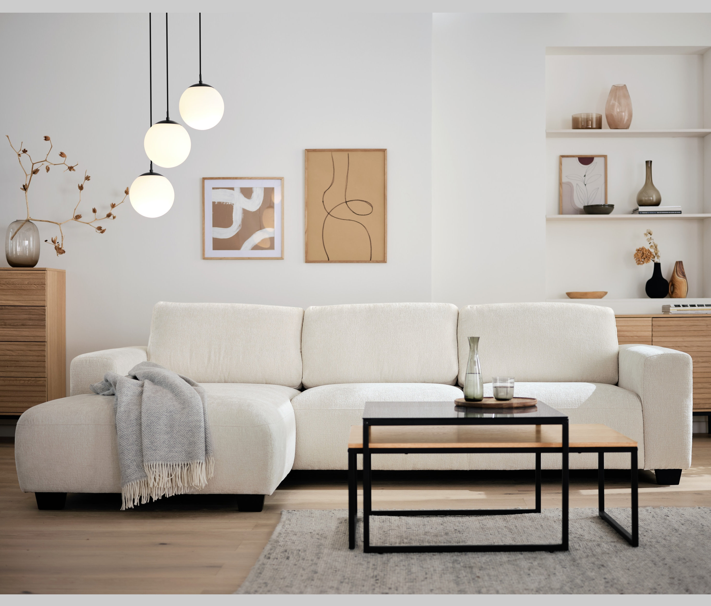 Ein Wohnzimmer mit einem cremefarbenen Ecksofa, einem zweiteiligen Couchtisch-Set und einer dreiflammigen Hängeleuchte mit Glaskugeln.