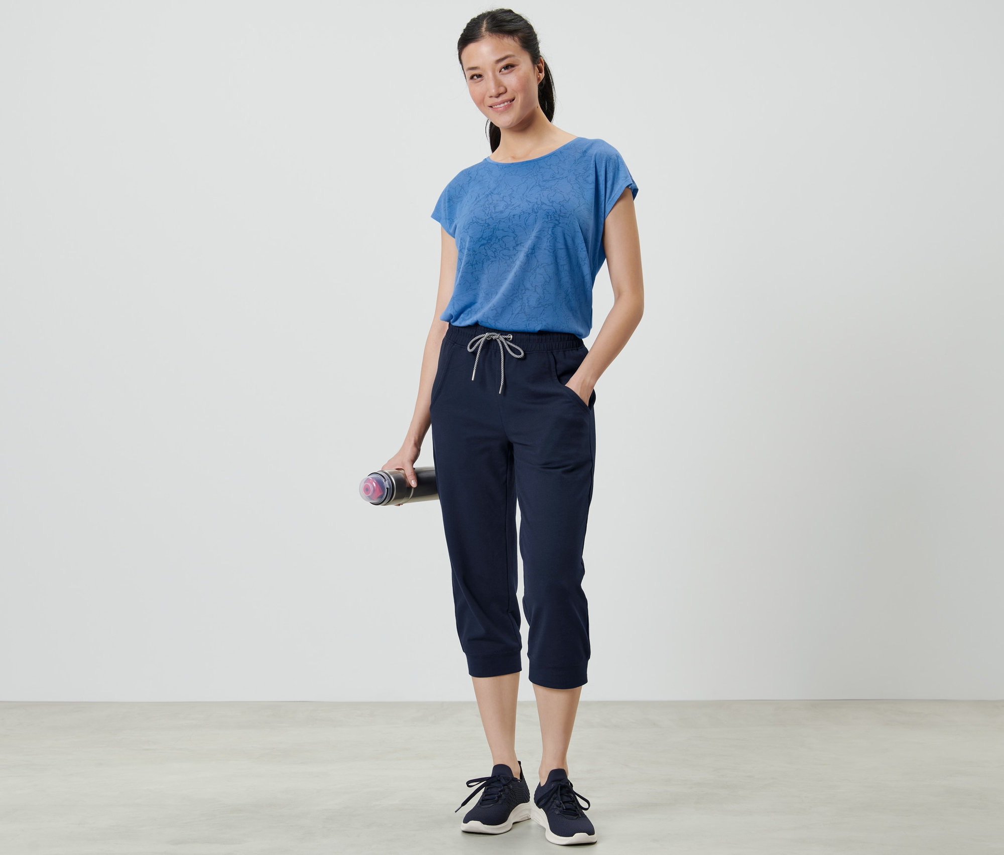 Frau hält eine Trainingsmatte und trägt eine 3/4-Sporthose.