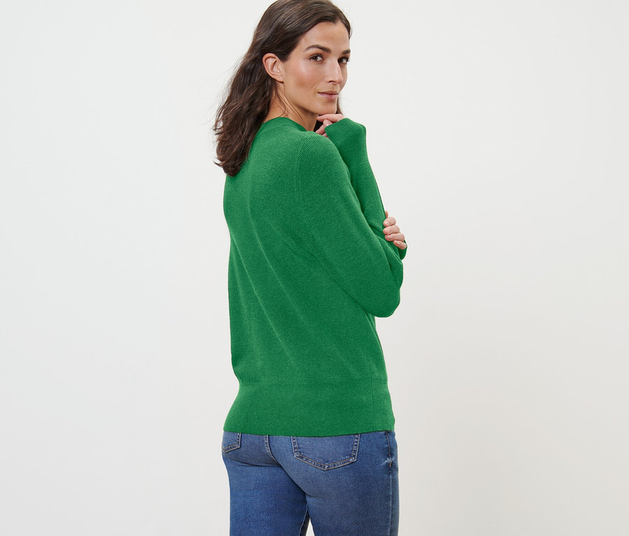 Frau blickt über die Schulter und trägt einen grünen Feinstrickpullover und Jeans.