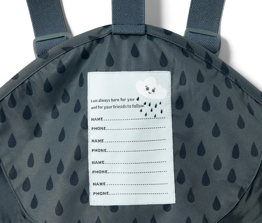 Detailaufnahme einer Kleinkind-Regenhose in Schieferblau mit Tropfenmuster und einem Etikett für Name und Telefonnummer.