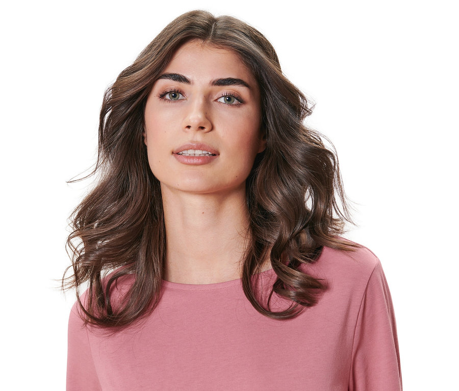 Porträt einer Frau mit gewellten braunen Haaren, die ein rosafarbenes Oberteil trägt. Haare mit hitzefreien Lockenwicklern gewellt.