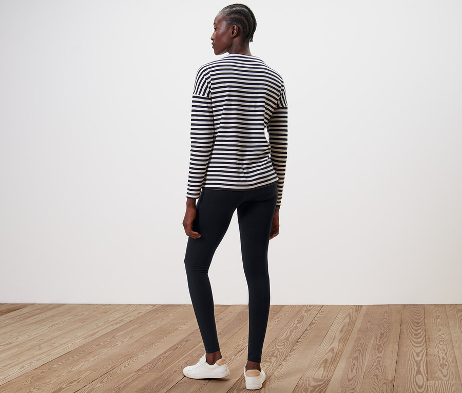 Frau steht mit dem Rücken zur Kamera und trägt schwarze Leggings und ein gestreiftes Oberteil.