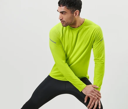 Mann dehnt sein Bein und trägt ein neonlimes Langarm-Funktionsshirt und schwarze Leggings.