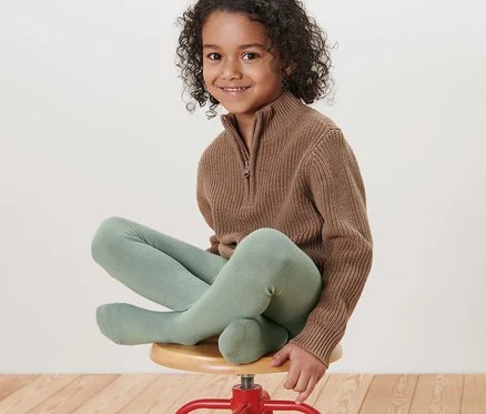 Ein Mädchen sitzt auf einem roten Hocker und trägt hellgrüne Kinder-Strumpfhosen.