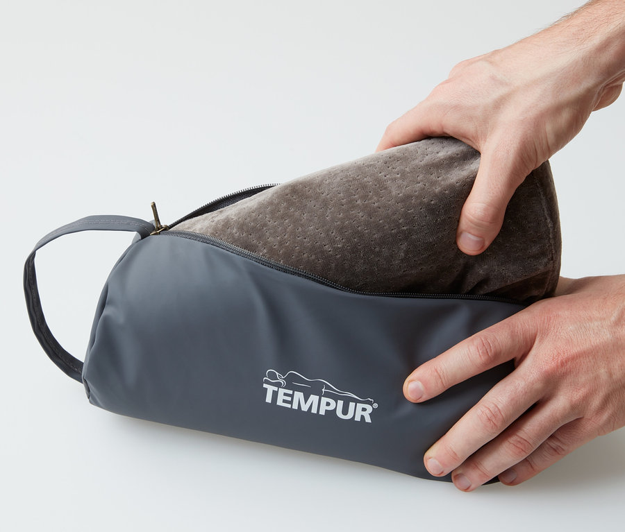 Hände nehmen ein braunes TEMPUR® Reisekissen aus einer grauen Tasche.