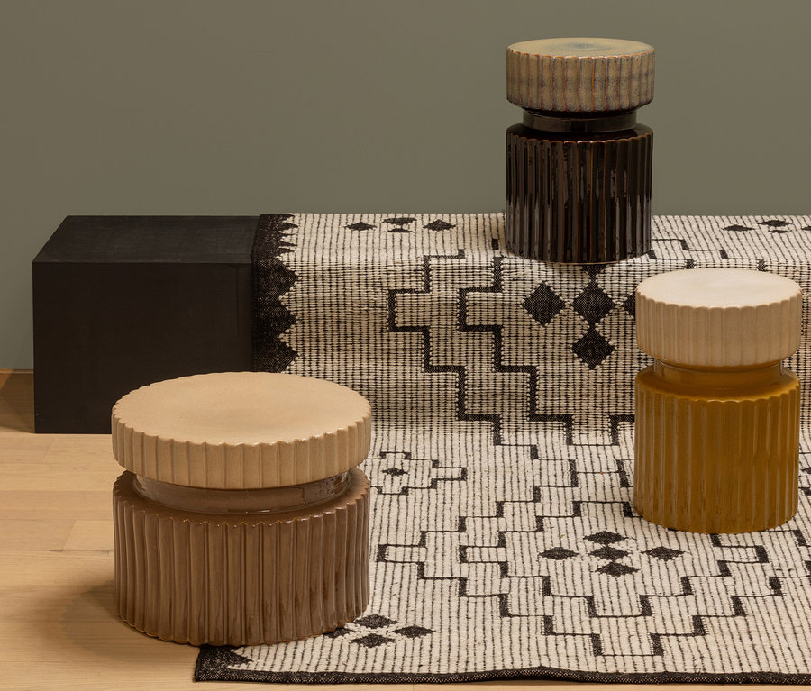 Drei braune und ockerfarbene Keramikhocker stehen auf einer schwarz-weiß gestreiften Decke. Sichtbar ist ein Woood Beistelltisch »Geer«, 38 x 48 cm, braun.