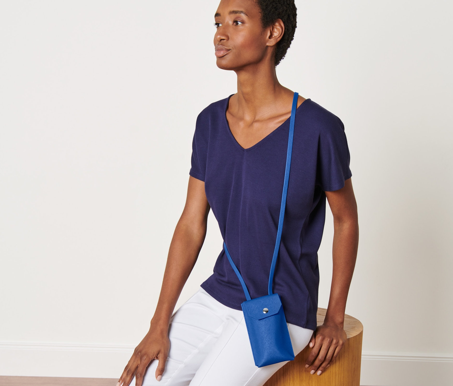 Frau sitzt auf einem Holzhocker und trägt eine blaue Mini-Tasche.